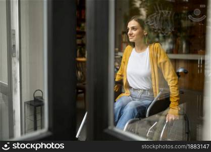 Disabled female student in wheelchair at the window, disability, bookshelf and university library interior on background. Handicapped young woman studying in college, paralyzed people get knowledge. Disabled female student in wheelchair at window