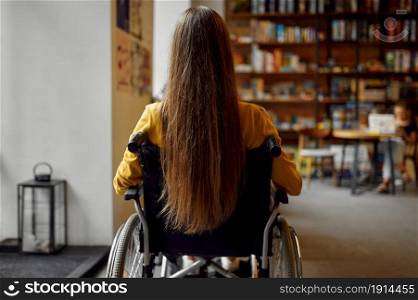 Disabled female student in wheelchair, back view, disability, bookshelf and university library interior on background. Handicapped young woman studying in college, paralyzed people get knowledge. Disabled female student in wheelchair, back view
