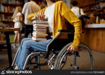 Disabled female student in wheelchair holds stack of books, disability, university library interior on background. Handicapped woman studying in college, paralyzed people get knowledge. Disabled female student holds stack of books