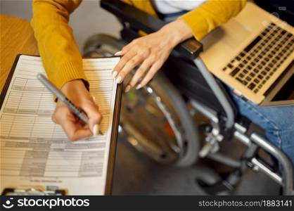 Disabled female student in wheelchair writes in notebook, disability, university library interior on background. Handicapped woman studying in college, paralyzed people get knowledge. Disabled student in wheelchair writes in notebook