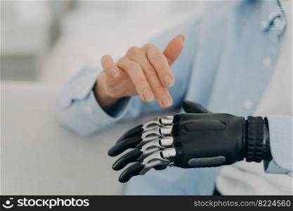 Disabled female training movements using bionic prosthesis of hand, touching, customizing artificial limb. Close up of womans healthy and prosthetic hands. Disability, high tech medical care concept.. Disabled female use prosthesis of hand, artificial limb, closeup. Disability, high tech medical care