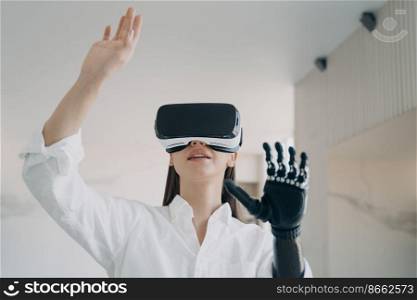 Disabled girl in virtual reality glasses touching 3d objects by robotic hand, testing new bionic prosthetic arm. Contemporary high tech in medicine and healthcare. Rehabilitation after limb loss.. Disabled girl in vr glasses testing new bionic prosthetic arm. Rehabilitation after limb loss
