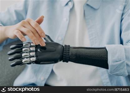 Disabled girl turns on her sensory bionic hand prosthesis, close up. Female with disability touches artificial robotic prosthetic arm. People with disabilities and high tech medical care concept.. Disabled female turns on sensory bionic hand prosthesis, close up. Medical high tech and disability