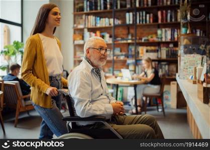 Disabled grandfather in wheelchair and granddaughter in cafe, disability, cafeteria interior on background. Handicapped older male person and young female guardian, paralyzed people in public places. Handicapped older male person and young guardian