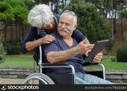 disabled husband in wheelchair using tablet in the park