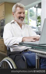 Disabled Man In Wheelchair Using Laptop At Home