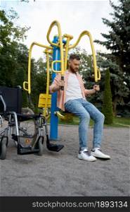 Disabled man on exercise machine in the park. Paralyzed people and disability difficulties, handicap overcoming. Handicapped male person on sport ground. Disabled man on exercise machine in the park