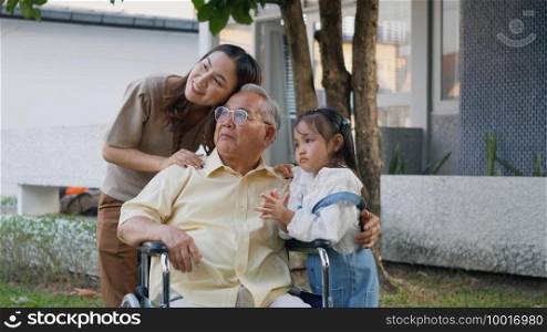 Disabled senior grandpa on wheelchair with grandchild and mother in park, Happy Asian three generation family having fun together outdoors backyard, Grandpa and little child smiling and laughed