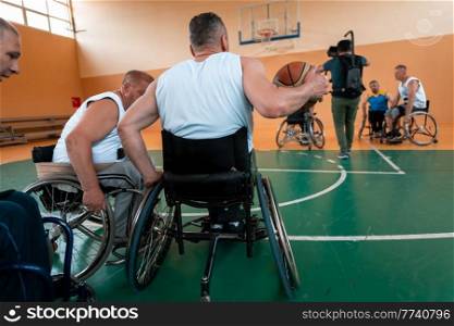 Disabled War or work veterans mixed race and age basketball teams in wheelchairs playing a training match in a sports gym hall. Handicapped people rehabilitation and inclusion concept.Hi quality photo. Disabled War veterans mixed race and age basketball teams in wheelchairs playing a training match in a sports gym hall. Handicapped people rehabilitation and inclusion concept