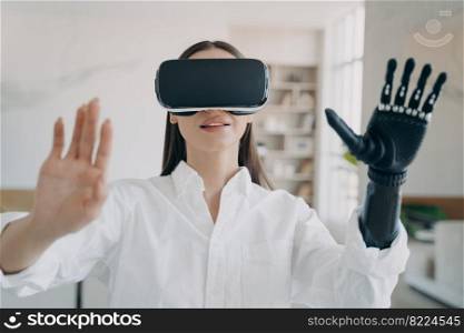 Disabled woman in virtual reality glasses touches objects by bionic prosthetic arm, interact with 3d cyberspace. Happy girl in VR goggles testing new device, training to use her artificial limb.. Disabled girl in virtual reality glasses touches objects training to use bionic prosthetic arm
