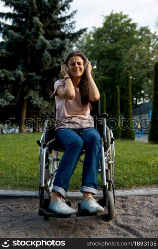 Disabled woman in wheelchair listens to music with headphones. Paralyzed people and disability, handicap overcoming. Handicapped female person walking in park. Disabled woman in wheelchair listens to music