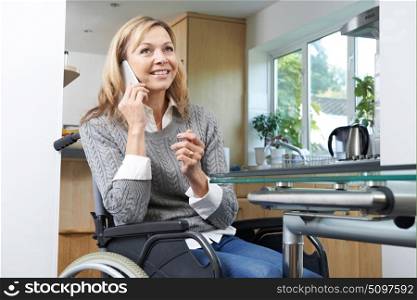 Disabled Woman In Wheelchair Making Call On Mobile Phone At Home