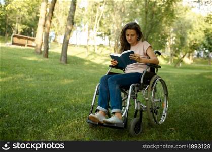 Disabled woman in wheelchair reading a book in park. Paralyzed people and disability, handicap overcoming. Handicapped female person leisures outdoors. Disabled woman in wheelchair reading book in park