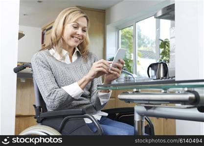 Disabled Woman In Wheelchair Texting On Mobile Phone At Home