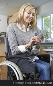 Disabled Woman In Wheelchair Texting On Mobile Phone At Home