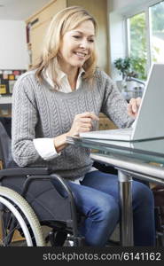 Disabled Woman In Wheelchair Using Laptop At Home