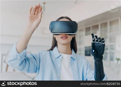 Disabled young girl wearing virtual reality glasses touches air by bionic prosthetic arm, female in new digital VR goggles playing using artificial hand. People with disabilities and medical high tech. Disabled girl in virtual reality glasses touching air by bionic prosthetic arm. Medical high tech