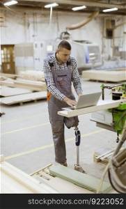Disabled young man with an artificial leg is working at the furniture factory