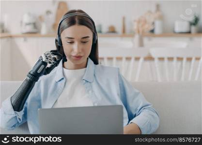 Disabled young woman in headset has online meeting with computer. European handicapped girl has equal rights. Remote manager at home on quarantine. Modern bionic prosthesis technology.. Disabled young woman in headset has online meeting with computer. Remote work.