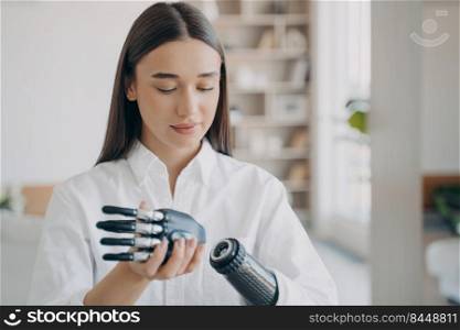 Disabled young woman is assembling bionic arm with hand. Prosthesis is connecting in wrist joint. Steel cyber hand has software and buttons, fingers and palm. Modern technology for wellbeing.. Disabled young woman is assembling bionic arm. Software and buttons, fingers and palm.
