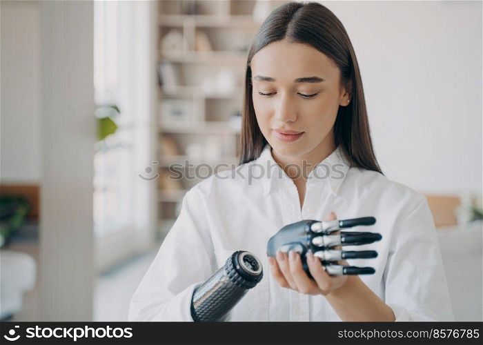 Disabled young woman is assembling bionic arm with hand. Prosthesis is connecting in wrist joint. Steel cyber hand has software and buttons, fingers and palm. Modern technology for wellbeing.. Disabled young woman is assembling bionic arm. Software and buttons, fingers and palm.
