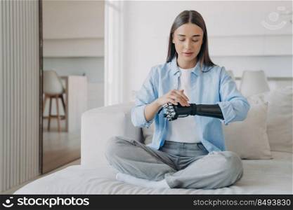 Disabled young woman is changing settings of bionic arm in morning. Cyber sensor hand has processor and buttons. European&utee adjusting electronic artificial arm at home. High tech carbon hand.. Disabled young woman is changing settings of bionic arm in morning. High tech carbon hand.