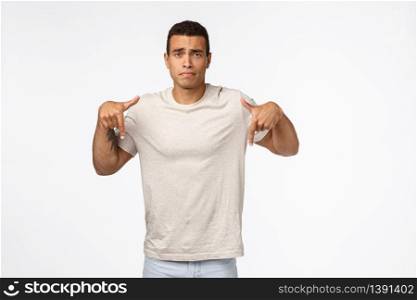 Disappointed, gloomy young tanned man in t-shirt, pointing down and looking upset, feeling displeased, distressed from seeing bad results, losing, failing exams, standing depressed white background.. Disappointed, gloomy young tanned man in t-shirt, pointing down and looking upset, feeling displeased, distressed from seeing bad results, losing, failing exams, standing depressed white background