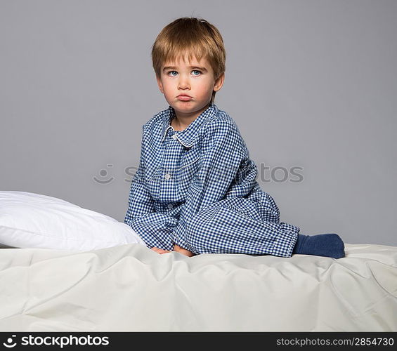 Disappointed little boy in blue pyjamas on bed