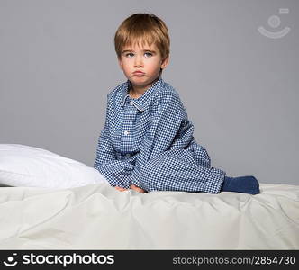 Disappointed little boy in blue pyjamas on bed