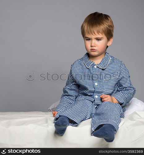 Disappointed little boy in blue pyjamas on bed