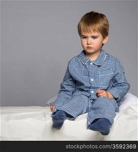 Disappointed little boy in blue pyjamas on bed
