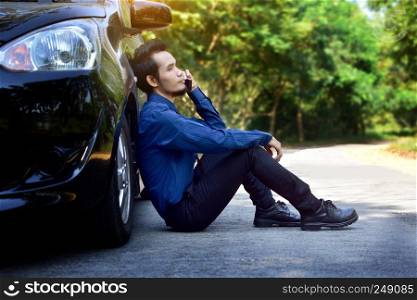 Disappointed man holding smart phone and sitting at car parked on road