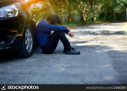 Disappointed man holding smart phone and sitting at car parked on road