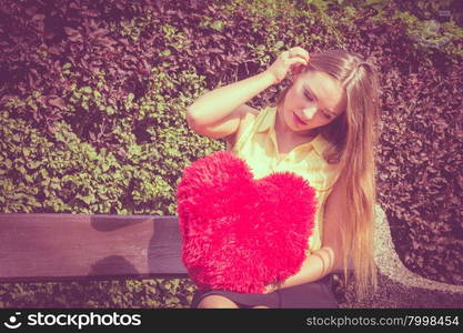 Disappointed woman with big red heart. Love and feelings. Unhappy hurt woman sitting on bench with big red heart in hands. Beautiful sad girl in park.