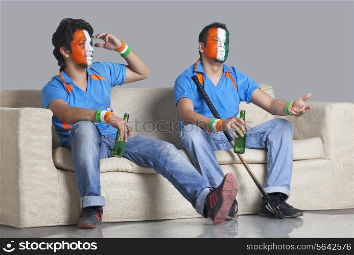 Disappointed young male friends with painted face looking away while holding bottle