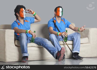 Disappointed young male friends with painted face looking away while holding bottle