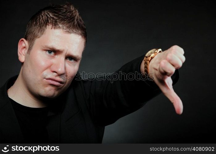 disappointed young man showing thumb down hand sign looking with negative expression disapproval on black background