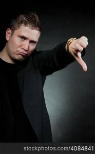 disappointed young man showing thumb down hand sign looking with negative expression disapproval on black background