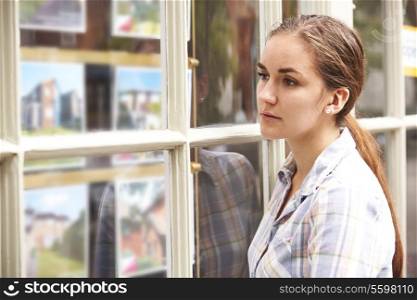 Disappointed Young Woman Looking In Window Of Estate Agents
