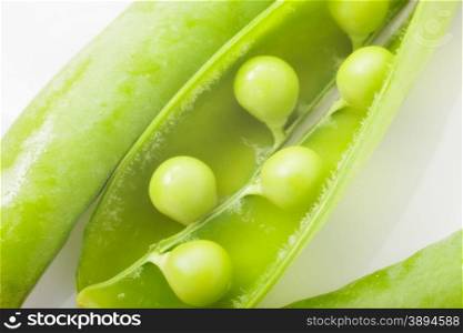 disclosed several pods of green peas on a white plate. close-up