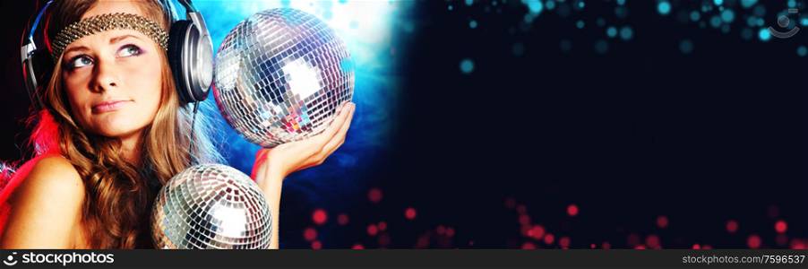Disco girl enjoys music in head phones holding mirror disco ball over black and colorful bokeh background. Disco girl enjoys music