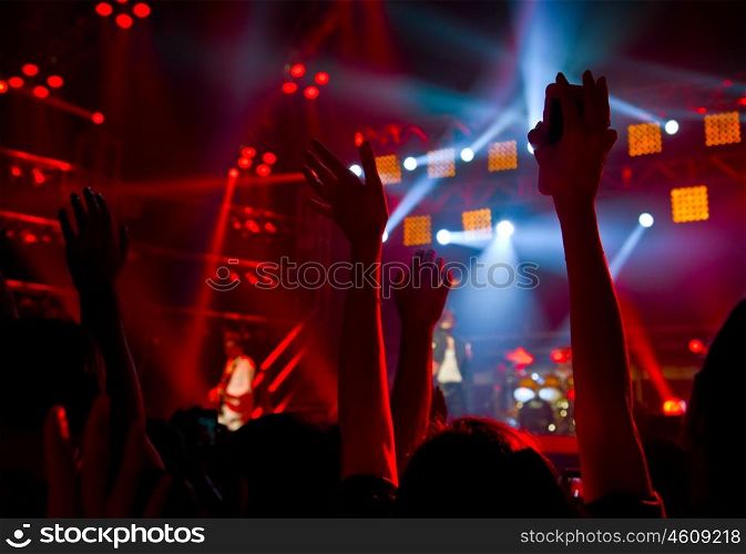 Disco party concert with large group of happy dancing people, silhouette of hands up in the air over blur red colorful stage lights, active lifestyle entertainment, music nightclub, night life concept