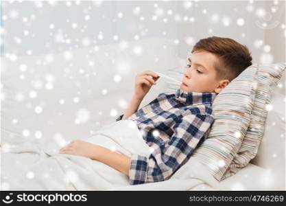 disease, healthcare and medicine concept - ill boy with flu measuring temperature by thermometer at home over snow