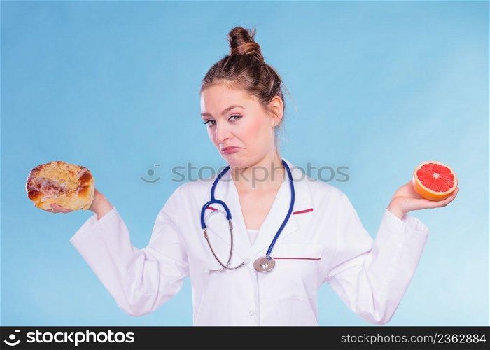 Disgusted dietitian nutritionist with sweet roll bun and grapefruit. Woman holding fruit and cake comparing junk and healthy food. Right eating nutrition concept.. Disgusted dietitian with sweet bun and grapefruit.