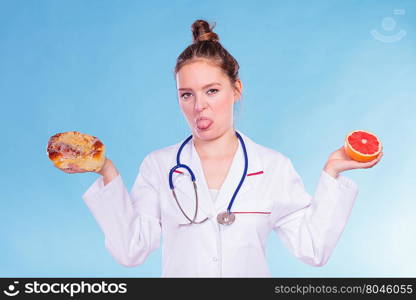 Disgusted dietitian with sweet bun and grapefruit.. Disgusted dietitian nutritionist with sweet roll bun and grapefruit. Woman holding fruit and cake comparing junk and healthy food. Right eating nutrition concept.