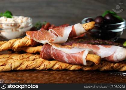Dish for Antipasto snacks with salami, bread sticks (Grissini) wrapped with prosciutto olives and cheese paste on the wooden surface