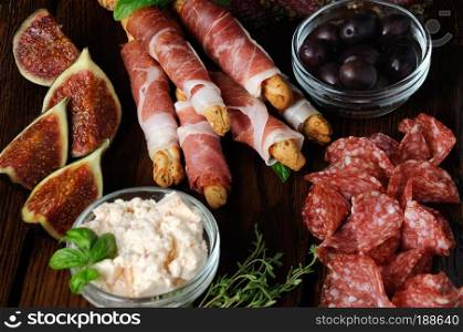 Dish for Antipasto snacks with salami, bread sticks wrapped with prosciutto  Grissini  olives and cheese paste on the wooden surface