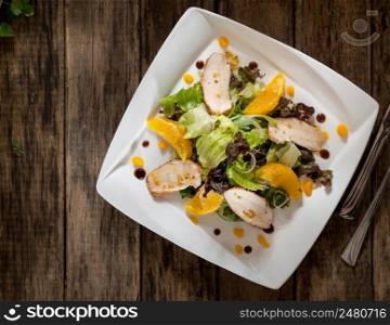 dish of chicken and salad in a white square plate on wooden boards, top view. dish on a wooden surface