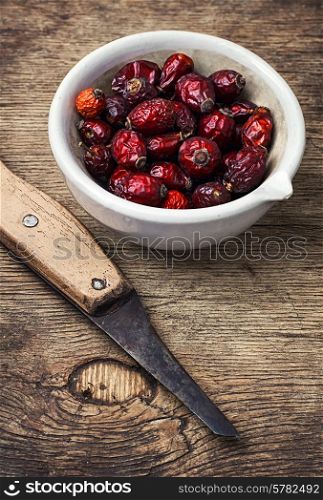 dish of dried medicinal rose hips on background of knife in rustic style. medicinal rose hips