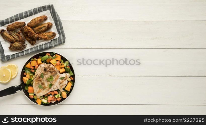 dish with chicken wings frying pan vegetables wooden desk